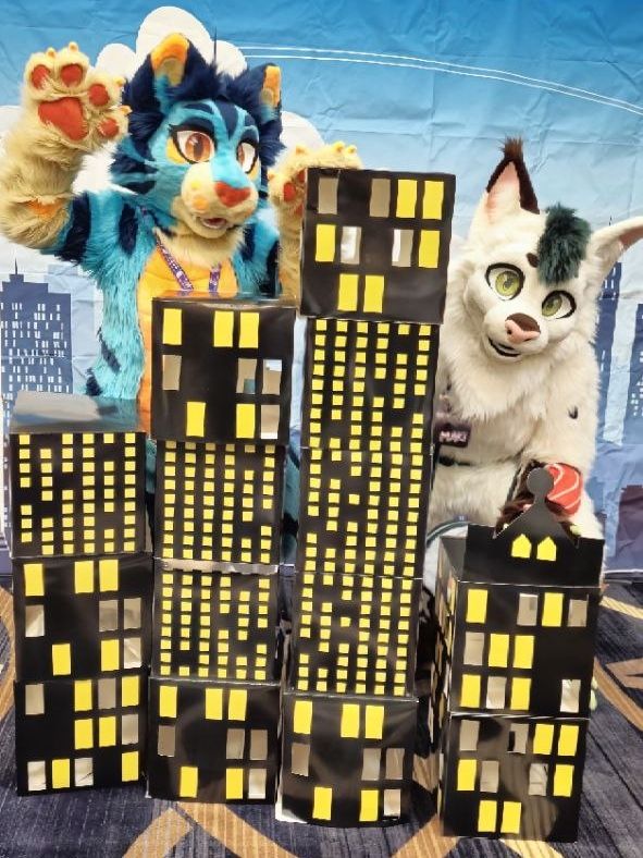 Two fursuits pose with miniature cardboard skyscrapers