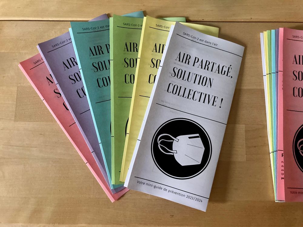 Covid prevention flyers titled “Air partagé, solution collective !” over a respirator. They’re printed on pink, purple, blue, green, yellow and white paper, and folded neatly.
