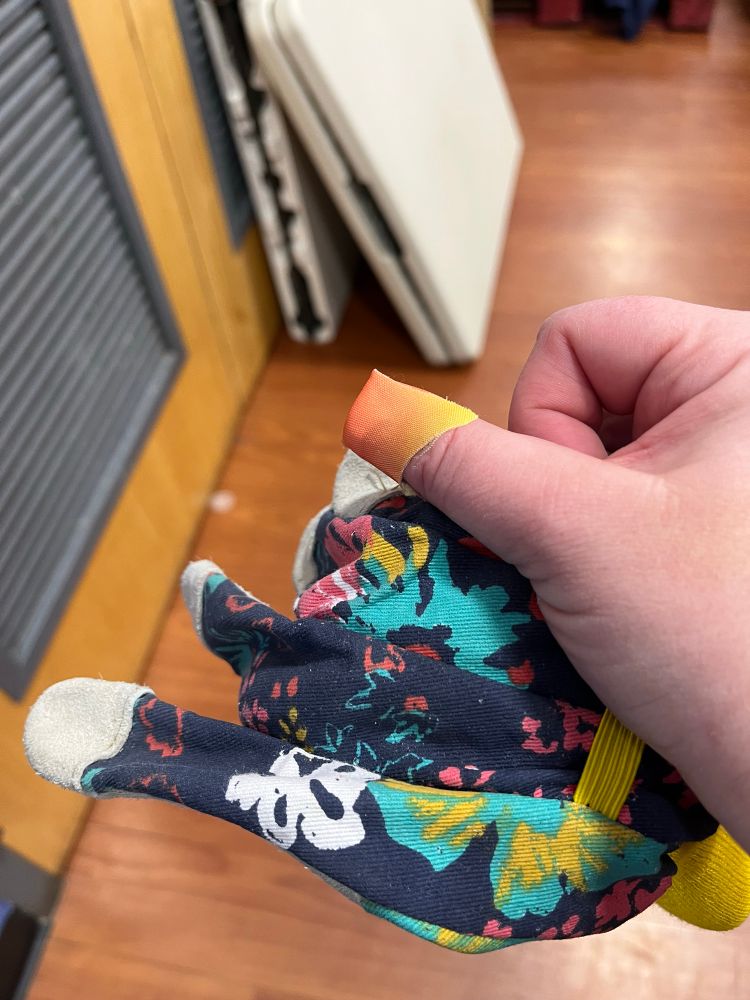 hand holding a pair of work gloves; there is a colorful bandaid on the thumb.