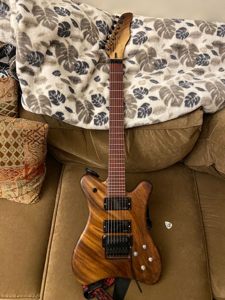 Brown wooden guitar on brown couch with blanket and pillow on couch 