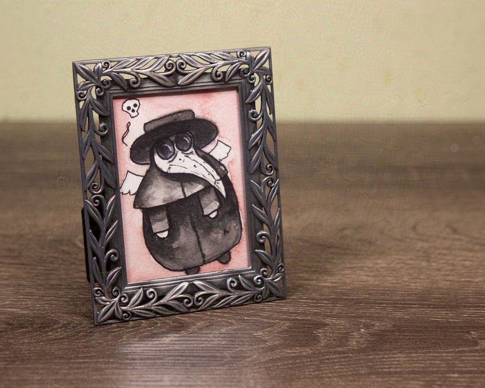 small watercolor painting of a 17th century plague doctor with a pink background. He's just a chubby little guy thinking about the afterlife. Framed in a small pewter frame with leaves and vines surrounding him.