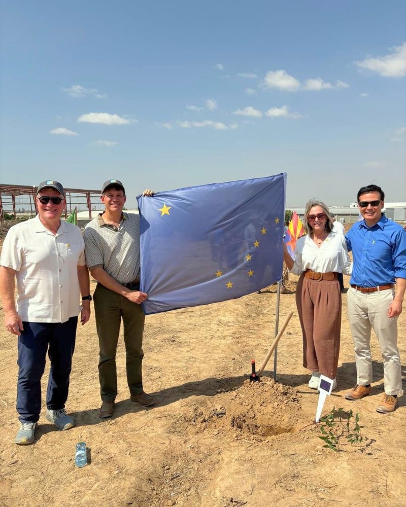 Four smiling people hold an Alaska flag in a desert environment
