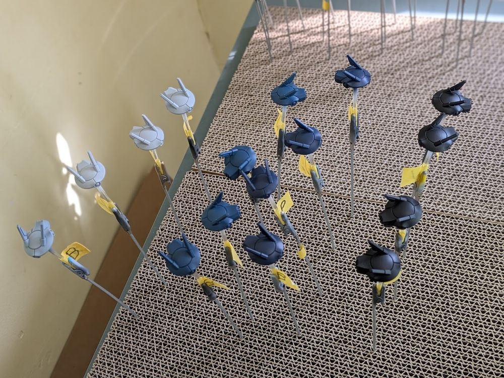 a collection of T'au drone proxies painted in 4 different colours each with 4 different primer coats. From left to right, off white, blue-grey, dark blue, blue-black