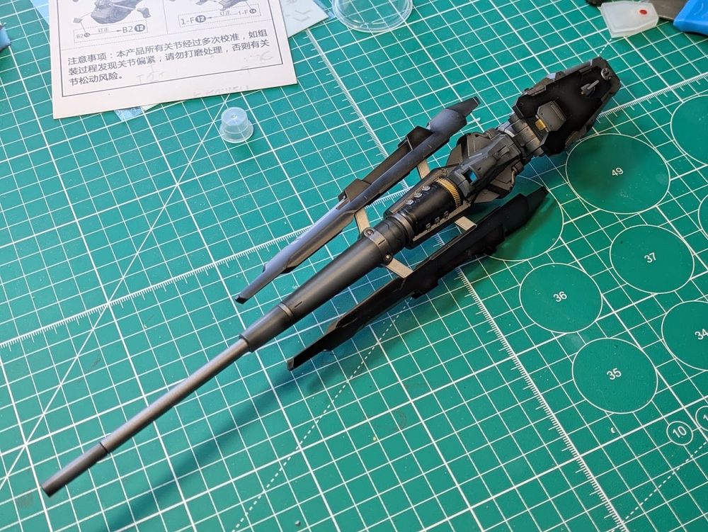 A large gun to be mounted on the right shoulder of the mobile suit it is dark grey and gunmetal with black and silver accents, the cowling is opened to reveal additional details