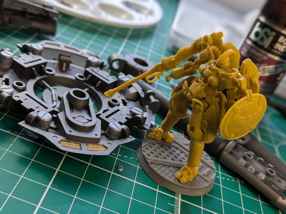 The inner frame of the Monument [Repair Type] shield laying on a cutting mat next to a Gundam Artifact Tallgeese to show the difference in scale 1/60 vs 1/285 (aproximately)