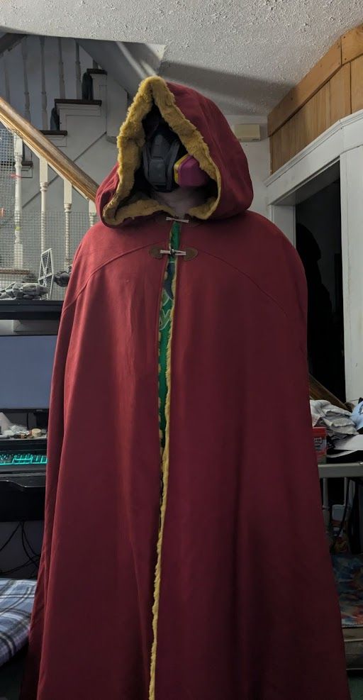 A man wearing a red cloak with pale gold trim and a respirator style filter mask who is definitely not thinking "From the moment I understood the weakness of my flesh, it disgusted me."