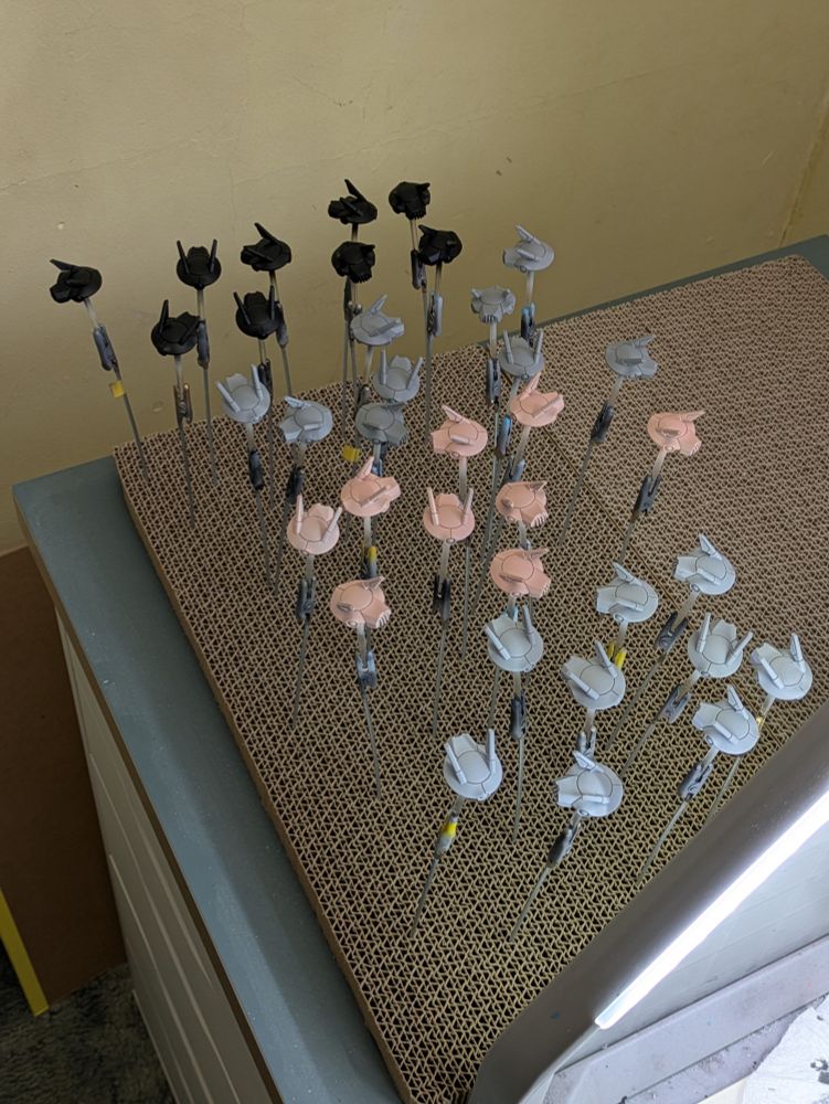 A collection of disk shaped drones with twin antennas on top, 36 in total. 9 each painted black, grey, pink, and white