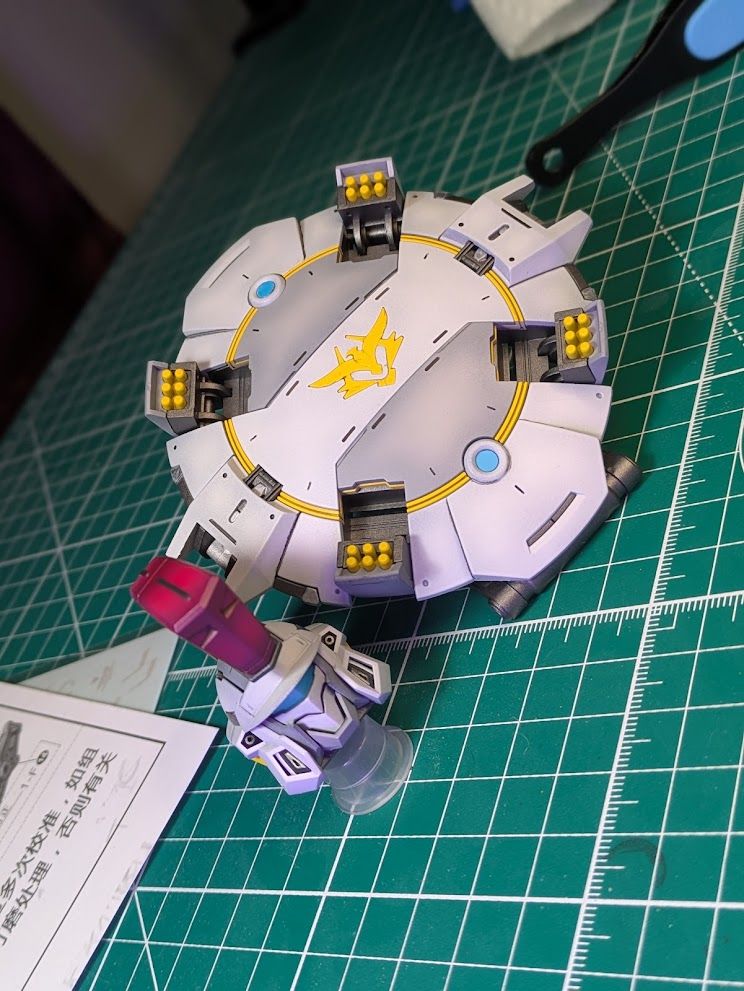 The head and shield from the Monument [Repair Type] 3rd party Tallgeese kit. Both are primarily white and grey but the shield has yellow accents including the warheads of missiles loaded into pods around the edge and  blue "lenses" and the helmet has a red crest and a blue "visor"