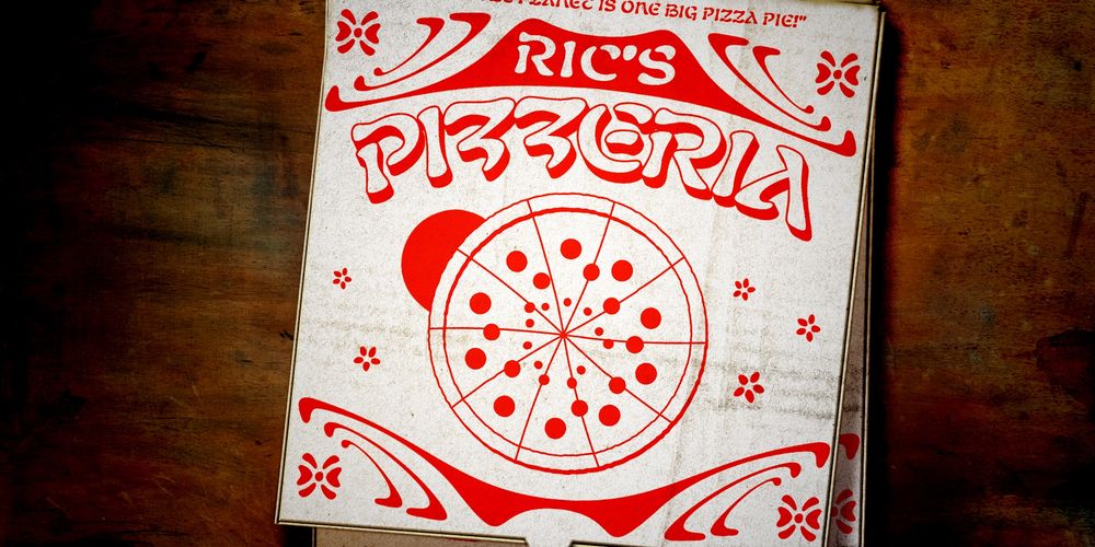 "RIC'S PIZZERIA" in printed on a stack of pizza boxes in Nabouveau Latin.