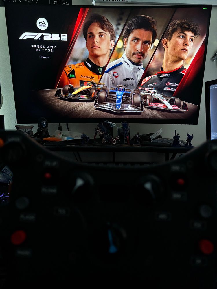 A picture of Xytrixz’s desk, with a steering wheel out of focus in the foreground and the F1 25 title screen in the background.