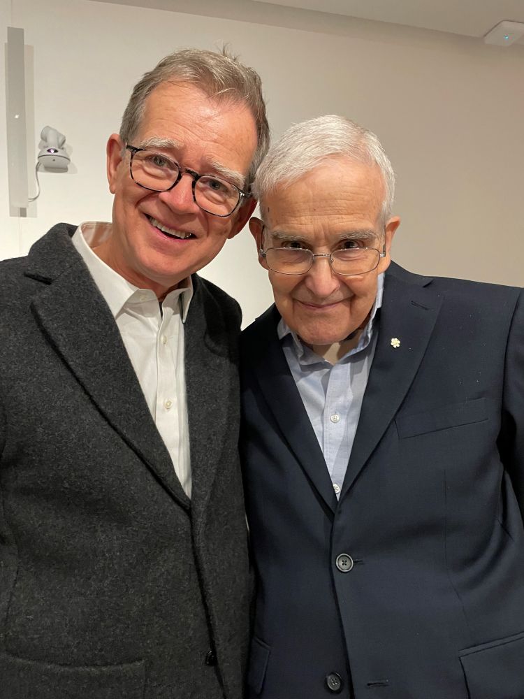 2 hommes portent des costumes noirs et des lunettes. 