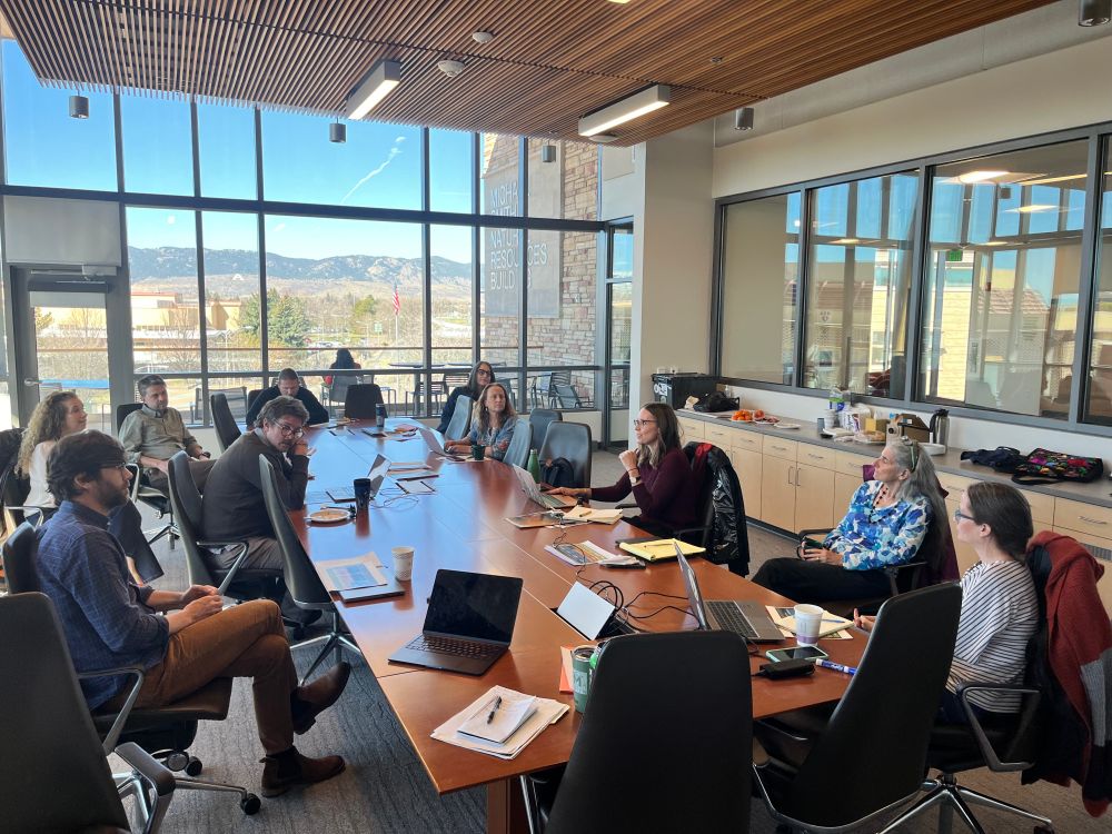 JSET meeting with many people sitting around a long wooden table discussing transdisciplinary research strategies. 