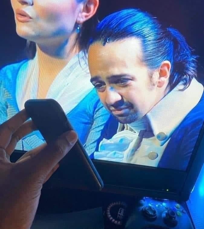 Lin manuel Miranda looks at a cellphone with concern 