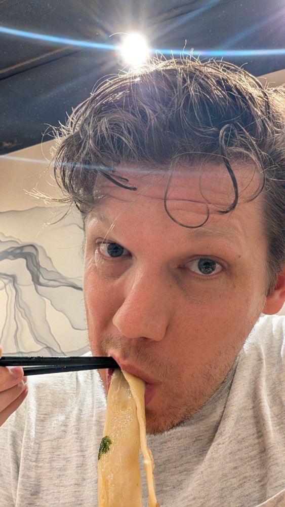 Brady is eating large flat noodles with a pair of chopsticks