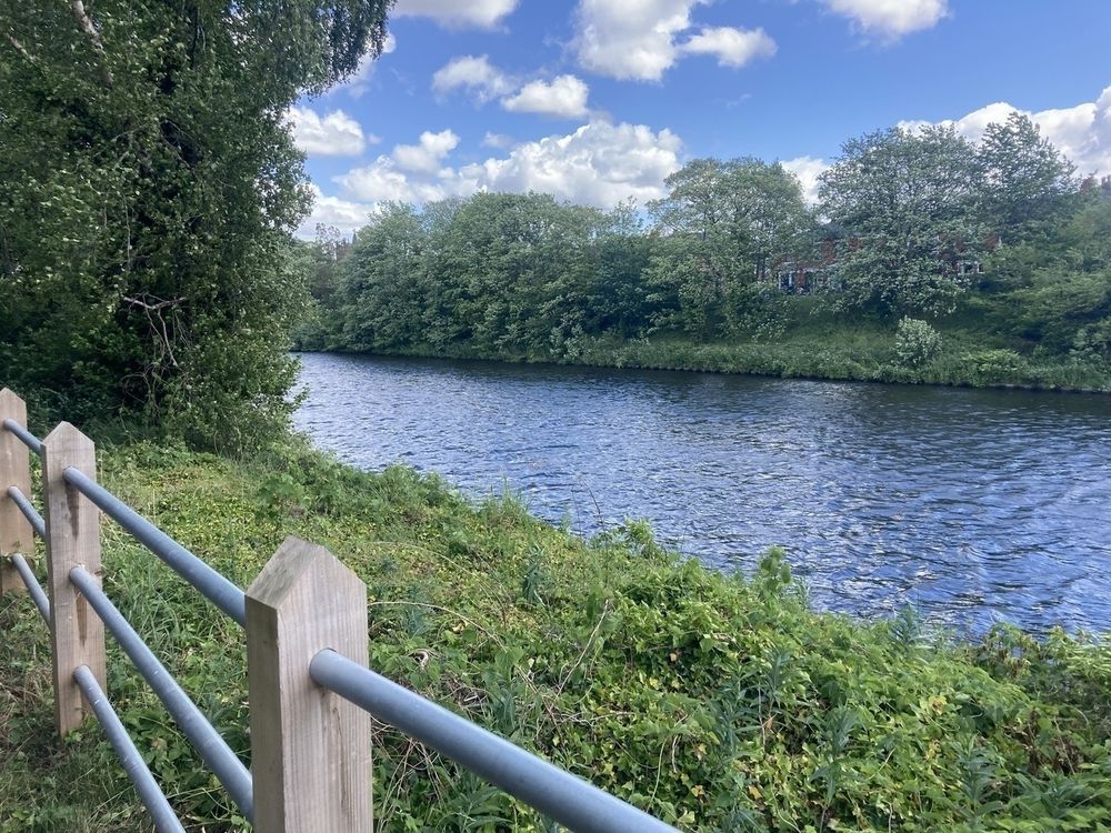 The Manchester Ship Canal with lush greenery on either bank. The sky is blue with little fluffy clouds