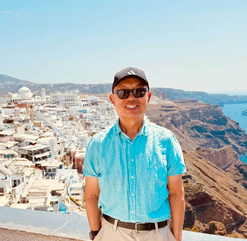 Photo of David Woo before a view of Santorini, Greece.