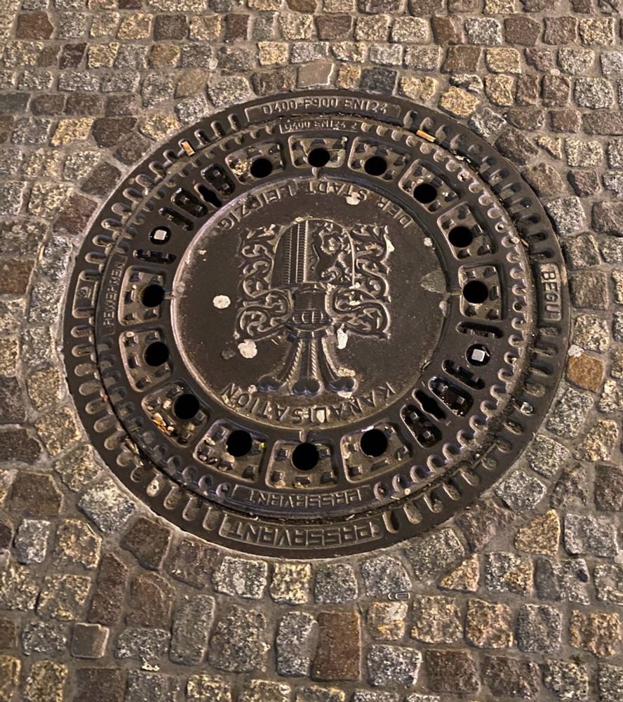 A photograph of a manhole cover with the Leipzig coat of arms embedded on it.