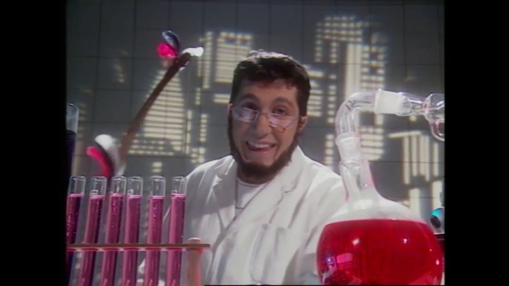 Alain Chabat dans son personnage du Professeur Thibaut, avec un un collier de barbe et des lunettes qui fait qu'il ressemble à Gendo Ikari d'Evangelion.