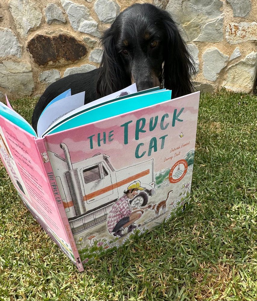 A black dachshund dog reading the ALIA NSS book “The Truck Cat”