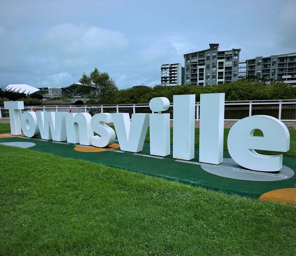 “Townsville” sign on grassy riverbank 