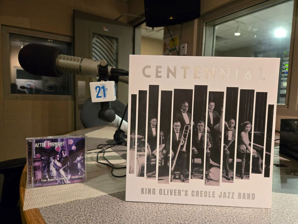 In front of a radio microphone with a 21st Show badge, the 2-CD set "After Midnight" by Ford Dabney's Syncopated Orchestras and the box set "Centennial" by King Oliver's Creole Jazz Band.