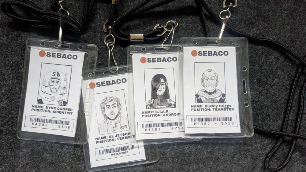 Four fictional employee badges of characters for the game Mothership. The characters work for the company "SEBACO". From left to right: DYRE COOPER, Scientist. AL JETTSON, Teamster. STAR, Android. BUCKLY BRIGGS, Teamster.