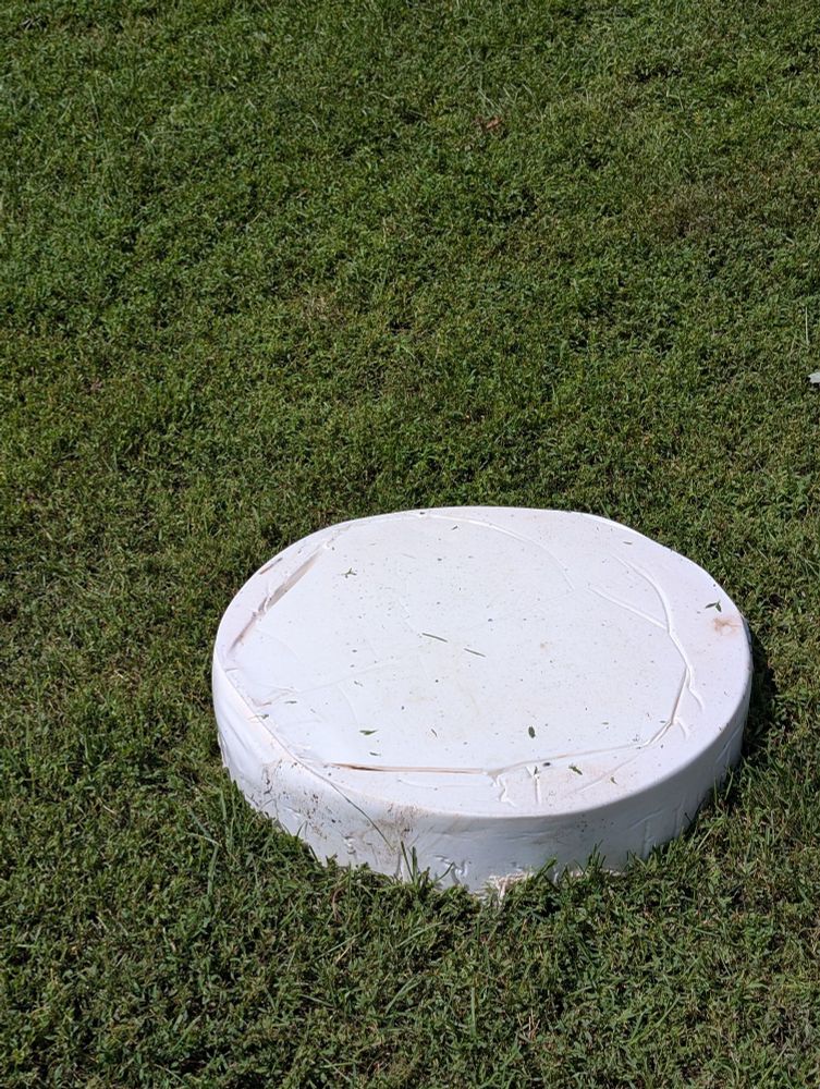 A white dense circle of dry PFA from the bottom of a 55 gallon drum of BMX track glue sitting in rough mown grass