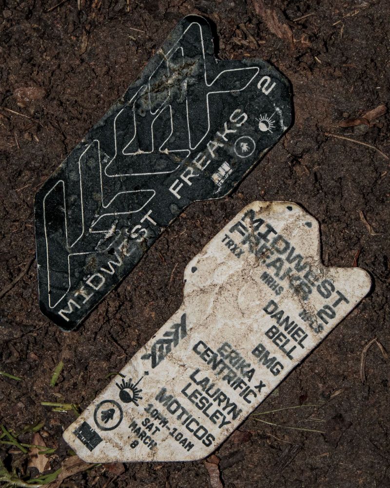 Rave flyer aesthetic image of stickers left in mud one side says "midwest freaks 2" other side lists lineup. Daniel Bell, BMG, Erika x Centrific, Lauryn Lesley, Moticos. 10pm-10am Sat March 8th.