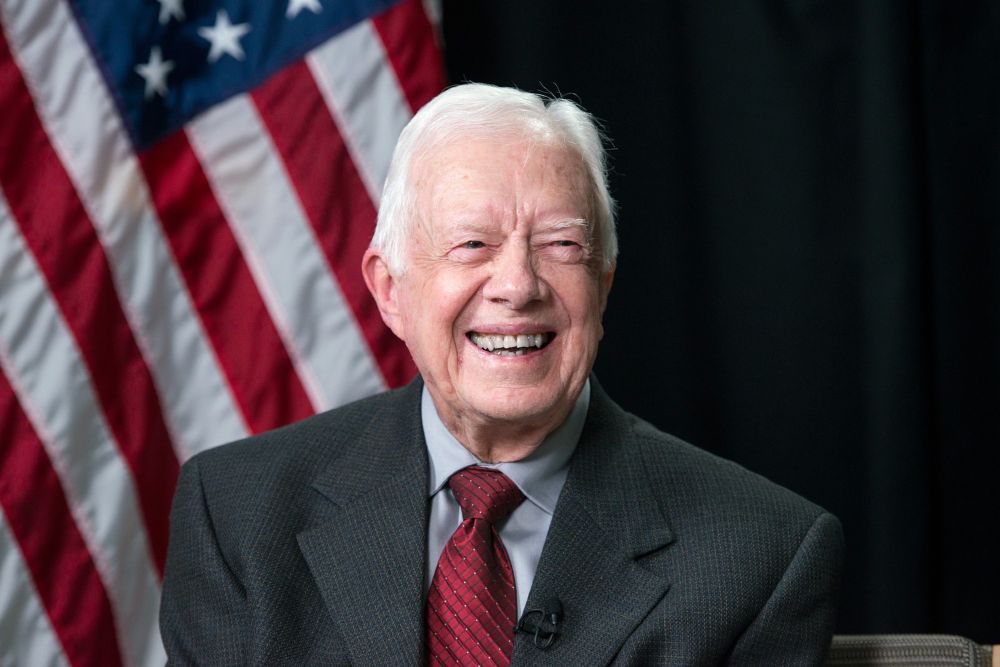 President Jimmy Carter, smiling in front of an American flag.Photo credit LBJ Library.