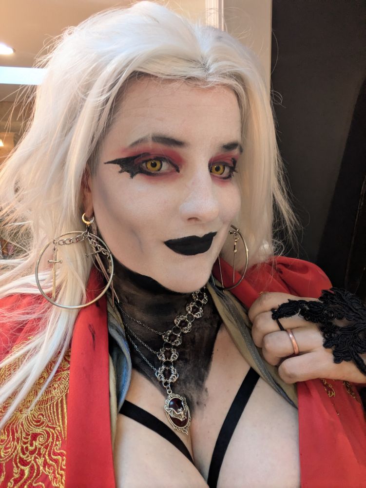 Profile picture of caffeinewitch in Gothic makeup. She has white hair, black gloves, and a red dress.