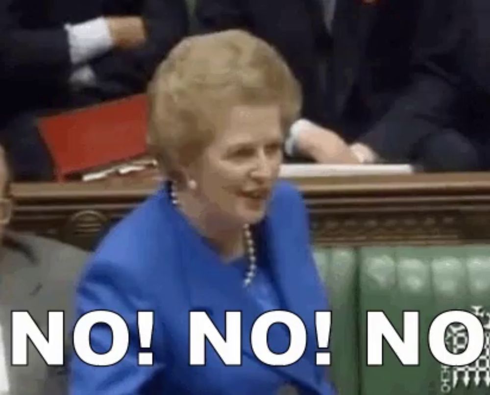 a woman in a blue suit is sitting in a parliament and says " no "