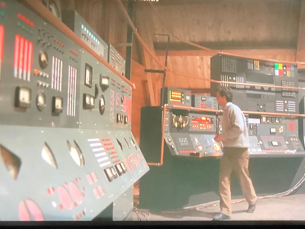Jef combs in from beyond stands in front of a bank of computers 