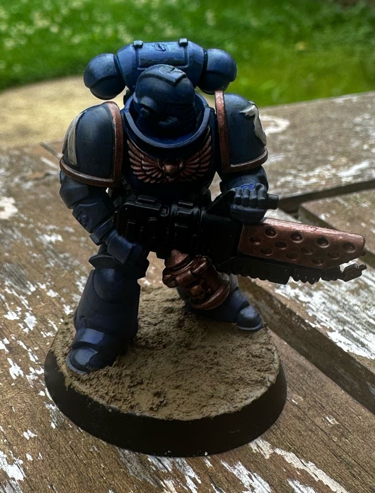 A blue Ultramarine Space Marine miniature, with sand gravel on the base and copper detailing on the flame thrower and insignia.