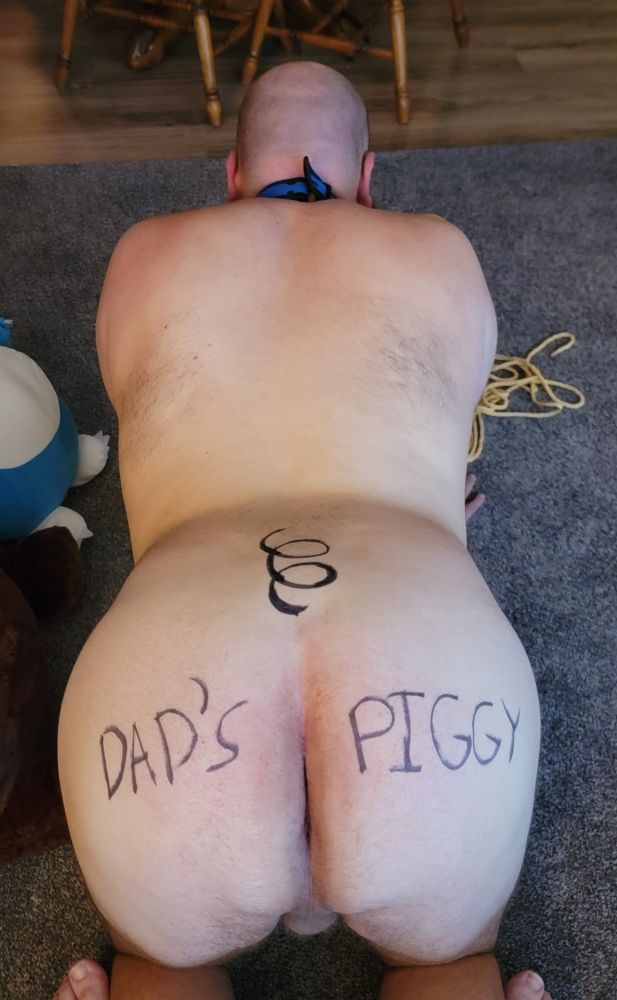 Bent over man with a pig tail and "Dad's Piggy" written on his butt
