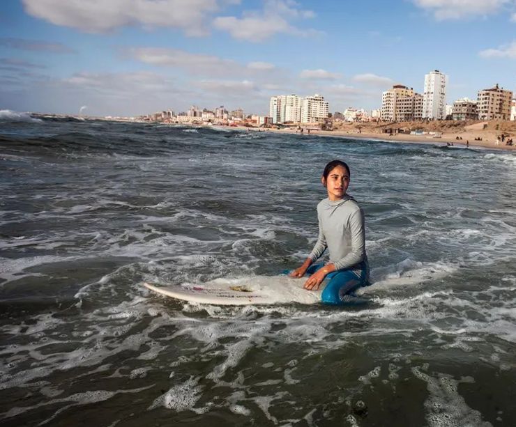 a girl on a surfboard, the Gaza beach and buildings in the background