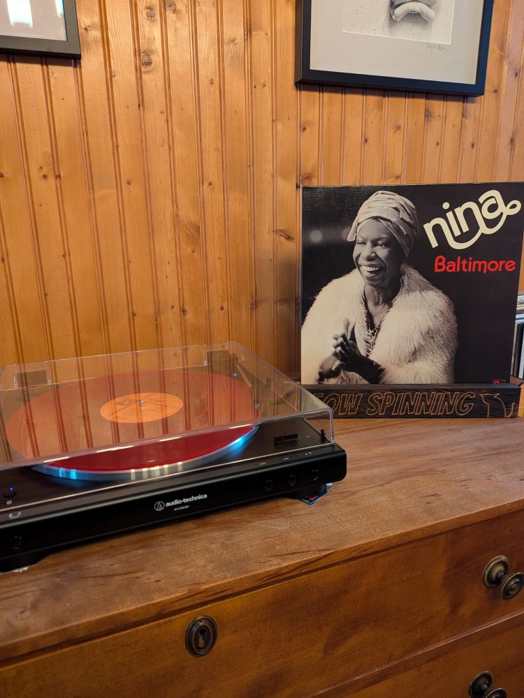 Turntable playing a red vinyl album. Album holder displaying Nina Simone's Baltimore.