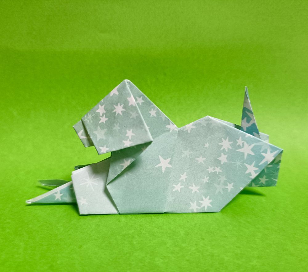 盲導犬のかたちに折った折り紙。色は薄い水色に白い星の柄が入ったもの。背景は黄緑色。