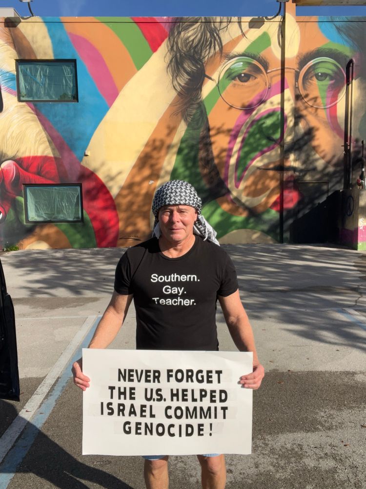 Me wearing keffiyeh standing in front of a mural of John Lennon 