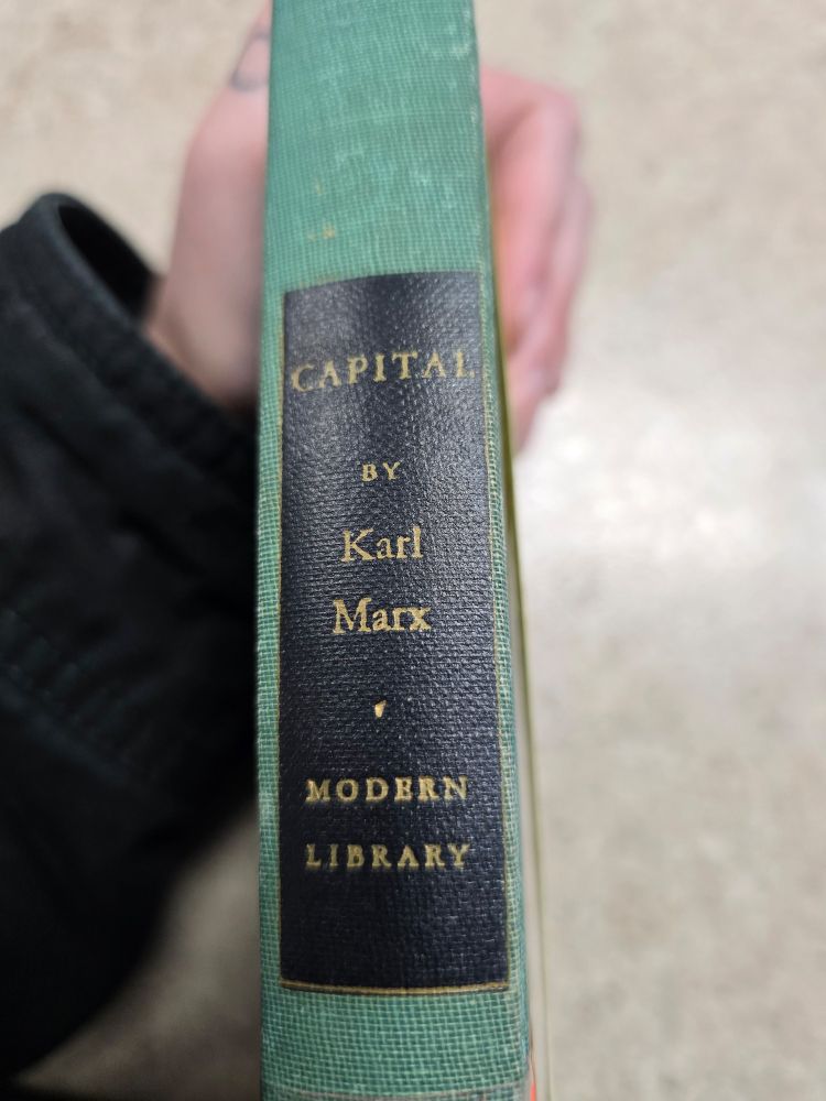 The side of a green book with a black rectangle with writing that says Capital by Karl Marx