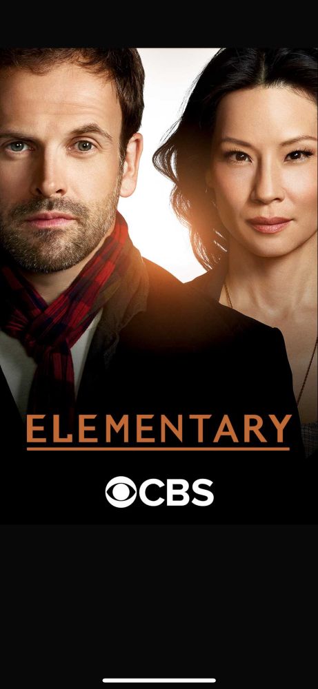 Elementary CBS Sherlock played by Jonny Lee Miller stands slightly in front of Watson played by Lucy Liu both facing forward 