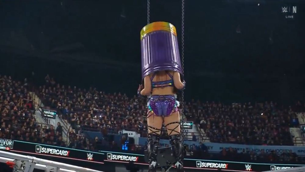 Iyo Sky atop the 2025 Wargames cage donning a trash can painted primarily purple except for a yellow/orange detailing round the bottom portion, about to perform her signature dive move at the associated event. #QueenShit #WearMeLikeAThrone