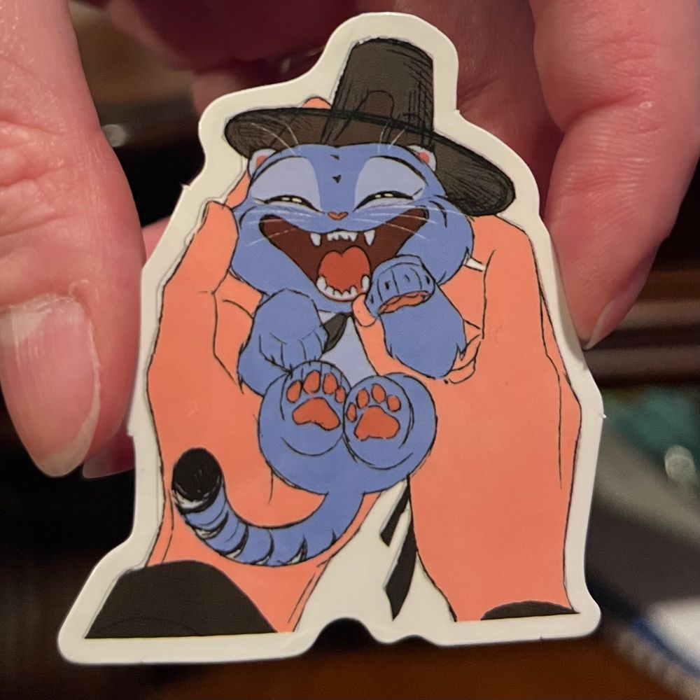 A sketched sticker or Derpy from K-POP Demon Hunters as a kitten being held in Jinu’s hands. 