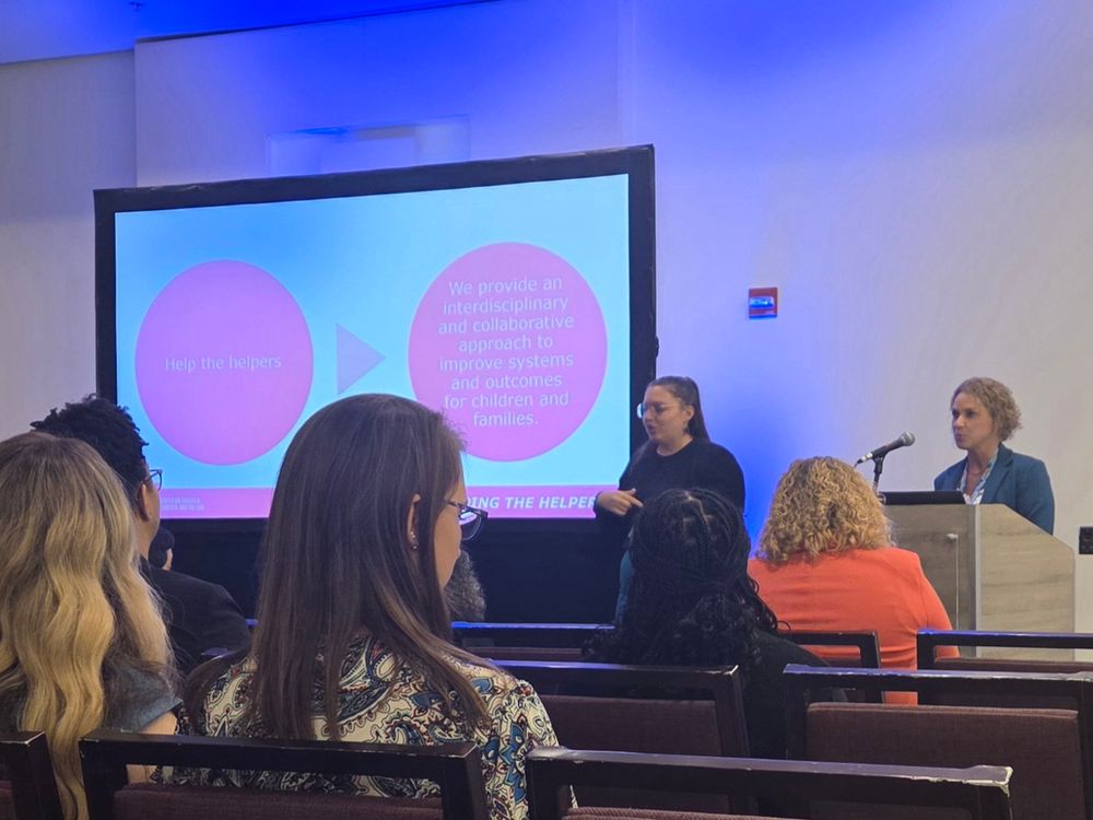 A woman presents at a podium next to a slide with two red circles