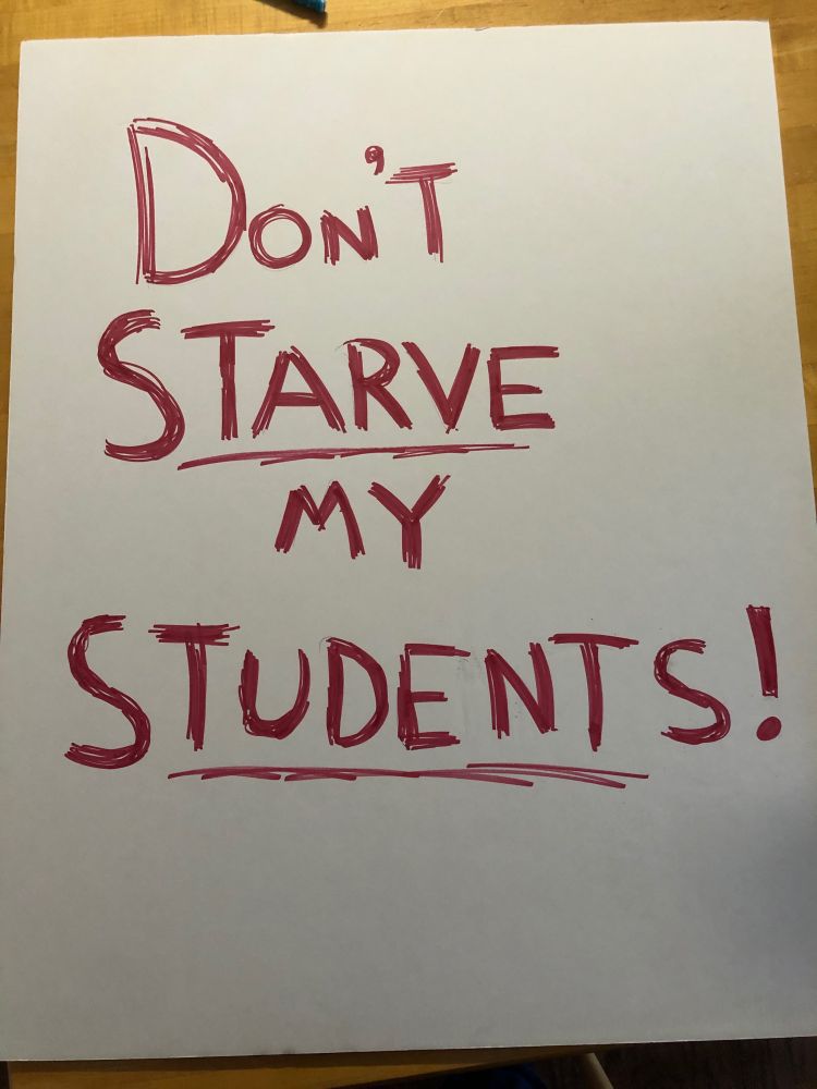 A white poster with “DON’T STARVE MY STUDENTS!” written in red marker.