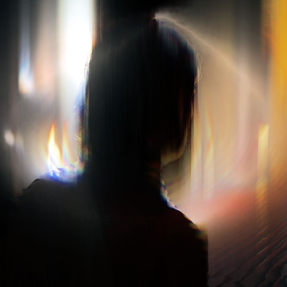 Virtual photography capture from Alan Wake 2. Alan Wake is viewed from behind, only his head and shoulders are visible. A strong light is pointed towards the camera on the left side of the image, creating a halo effect around Alan's head. The image is in color, but Alan is almost completely backlit , and the background is almost golden due to the yellow wallpaper and gold stanchion. The background is not only out of focus, but there is a heavy distortion across the image, giving it a dreamy effect opposite the clean look of the first image.