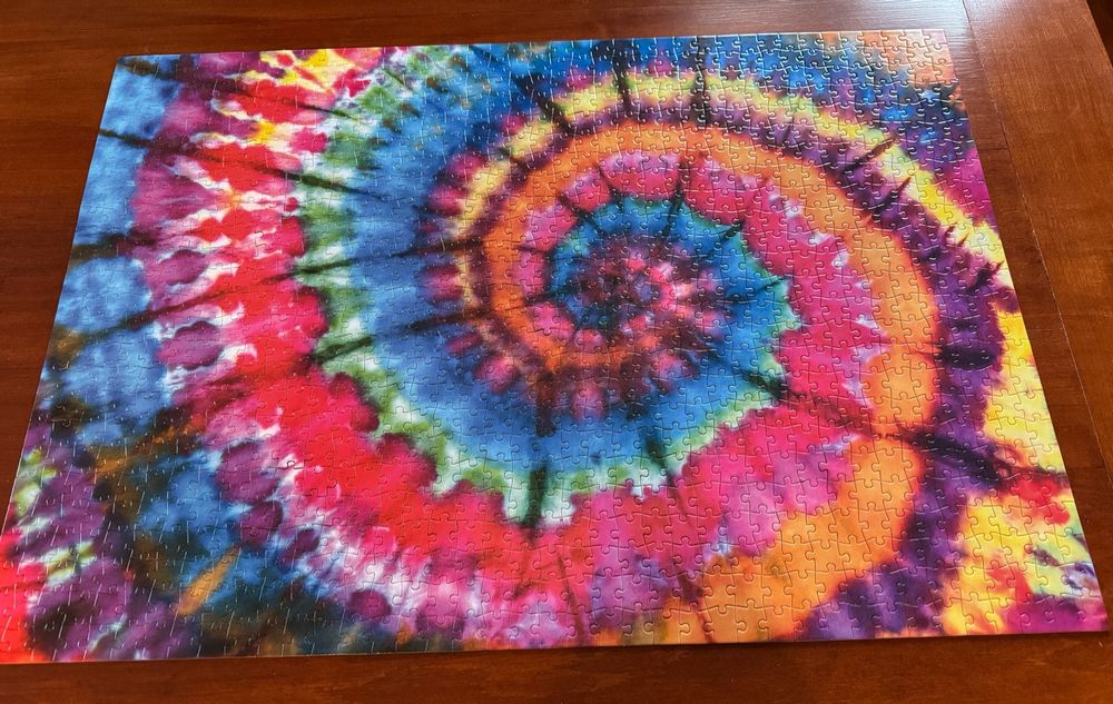 The completed puzzle, a tie-died swirl pattern with yellow, purple, orange, pink, green, and blue streaks spiraling around each other to the center. It is very colorful and beautiful. 