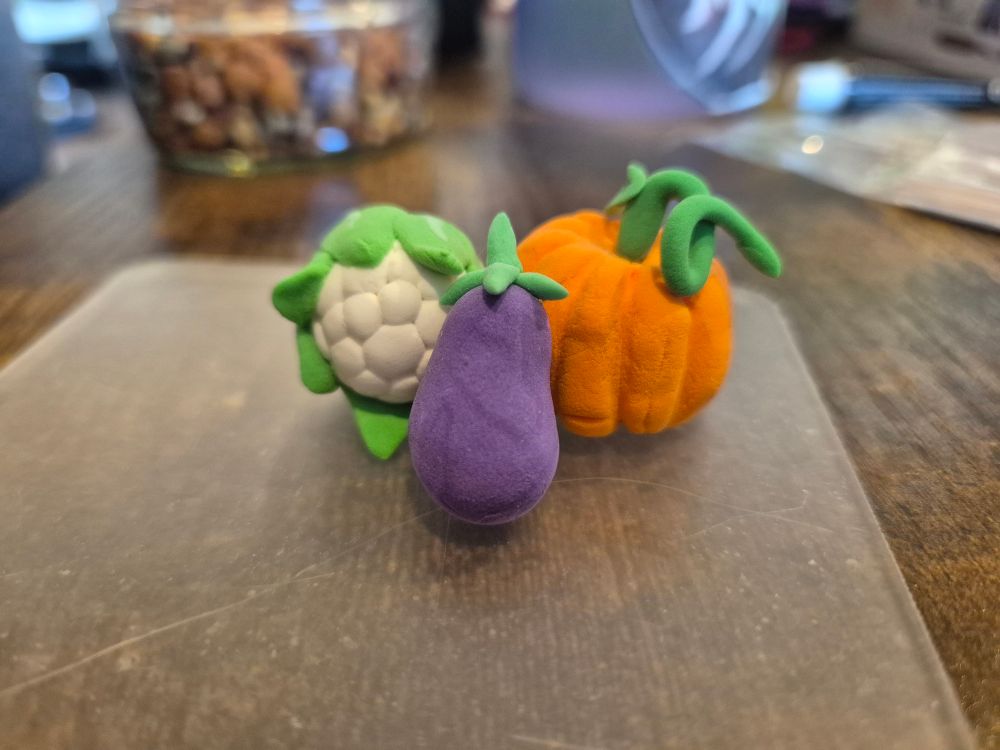 Small clay figurines depicting a cauliflower, eggplant and pumpkin.