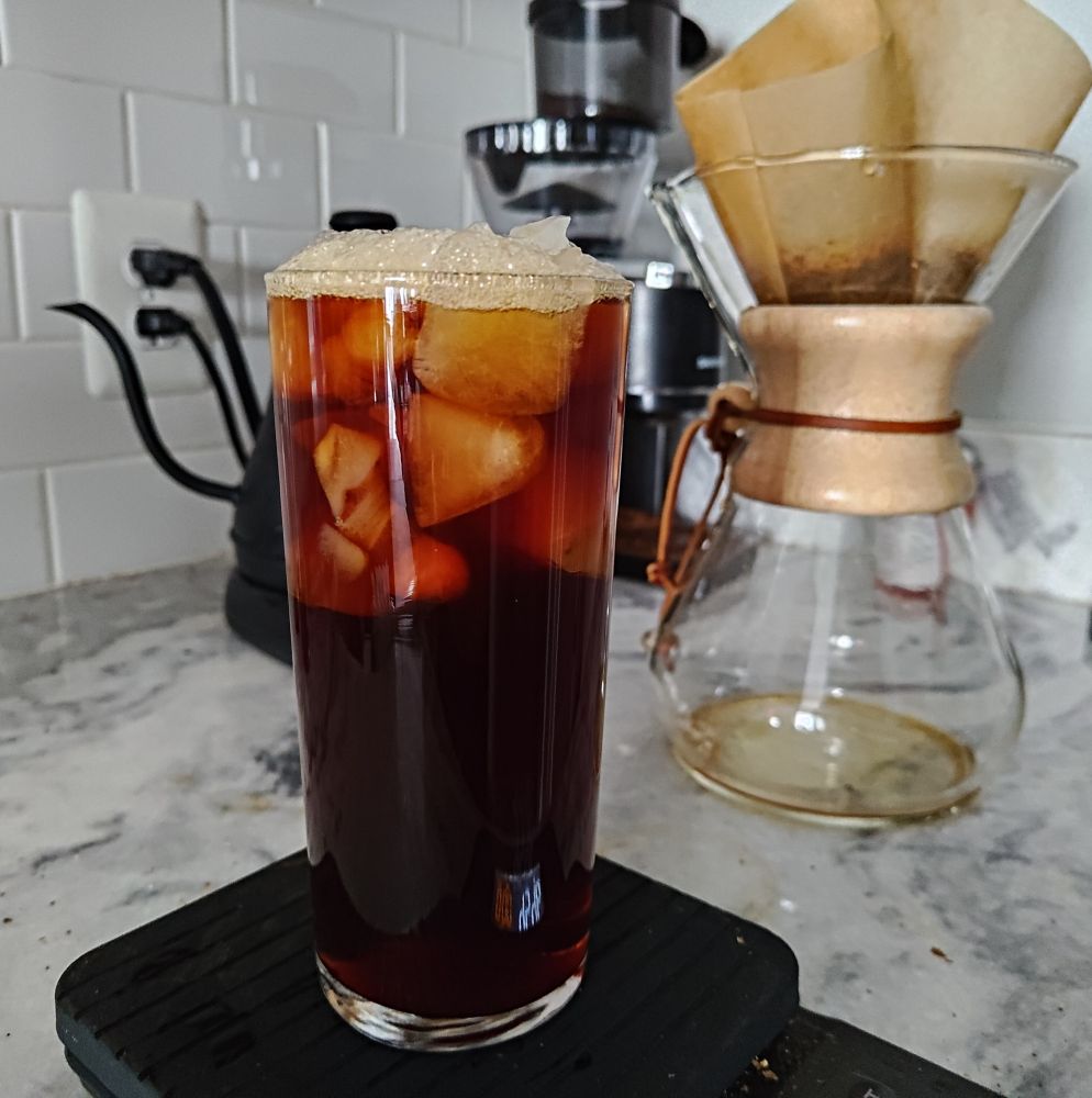 a bunch of coffee gear on a counter, in front a tall glass filled with iced coffee sitting on a scale

it looks delicious 