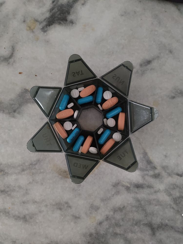a heptagonal pill holder with a slot for each day of the week, each slot filled with 4 pills of varying size and color.