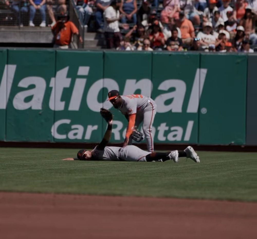 colton cowser lying in the ground holding his glove in the air as daniel johnson checks on him